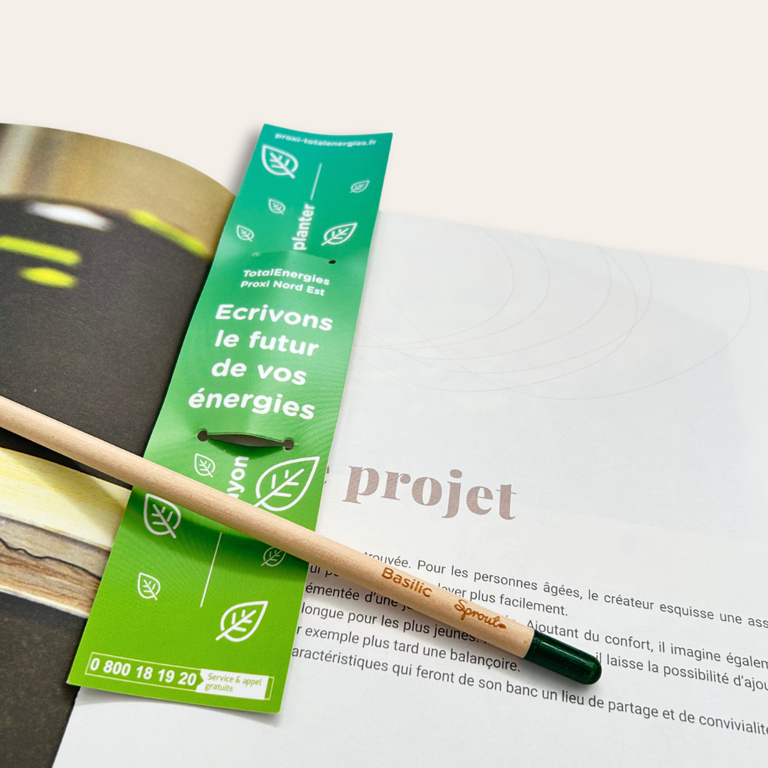 Crayon à planter personnalisable avec étui pour en faire un marque page Crayon de papier et étui personnalisé pour TotalEnergie posés sur un livre ouvert.