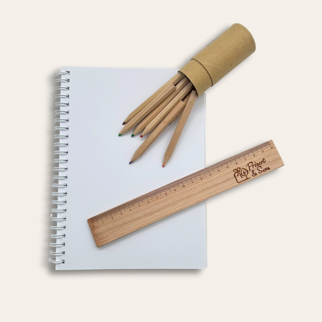 Règle en bois de 20cm Une règle en bois posée sur un cahier avec une boîte de crayons à côté.