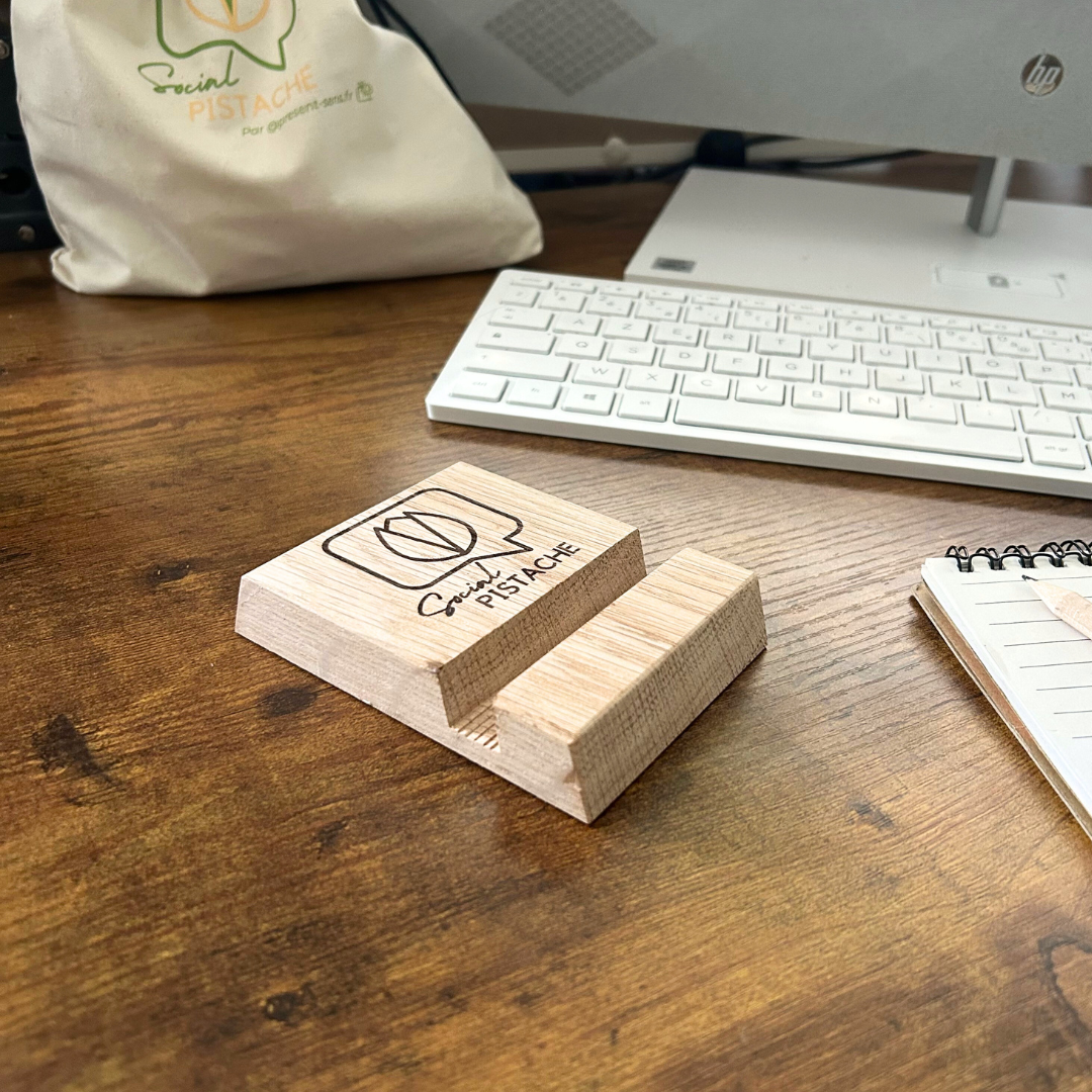 Support téléphone d'un bois gravé Social Pistache Support téléphone en bois gravé Social Pistache et un pochon et clavier en arrière-plan.
