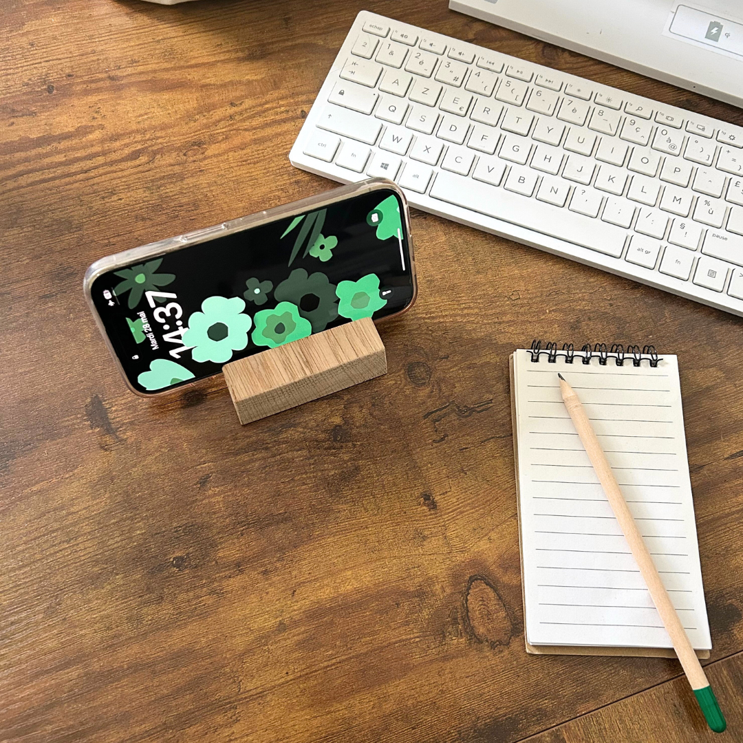 Support téléphone bois gravé et mobile en horizontal Support téléphone bois gravé avec mobile dessus en horizontal et un bloc note, crayon de bois et clavier sur le côté.