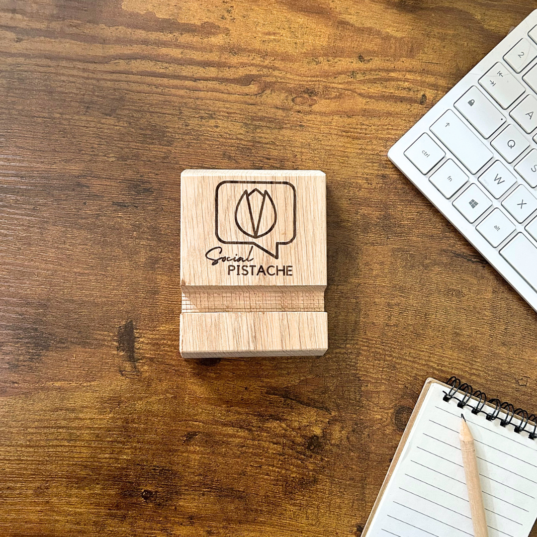 Support téléphone bois personnalisé d'un logo Support de téléphone en bois gravé au logo de Social Pistache avec bloc-notes et clavier sur le côté.
