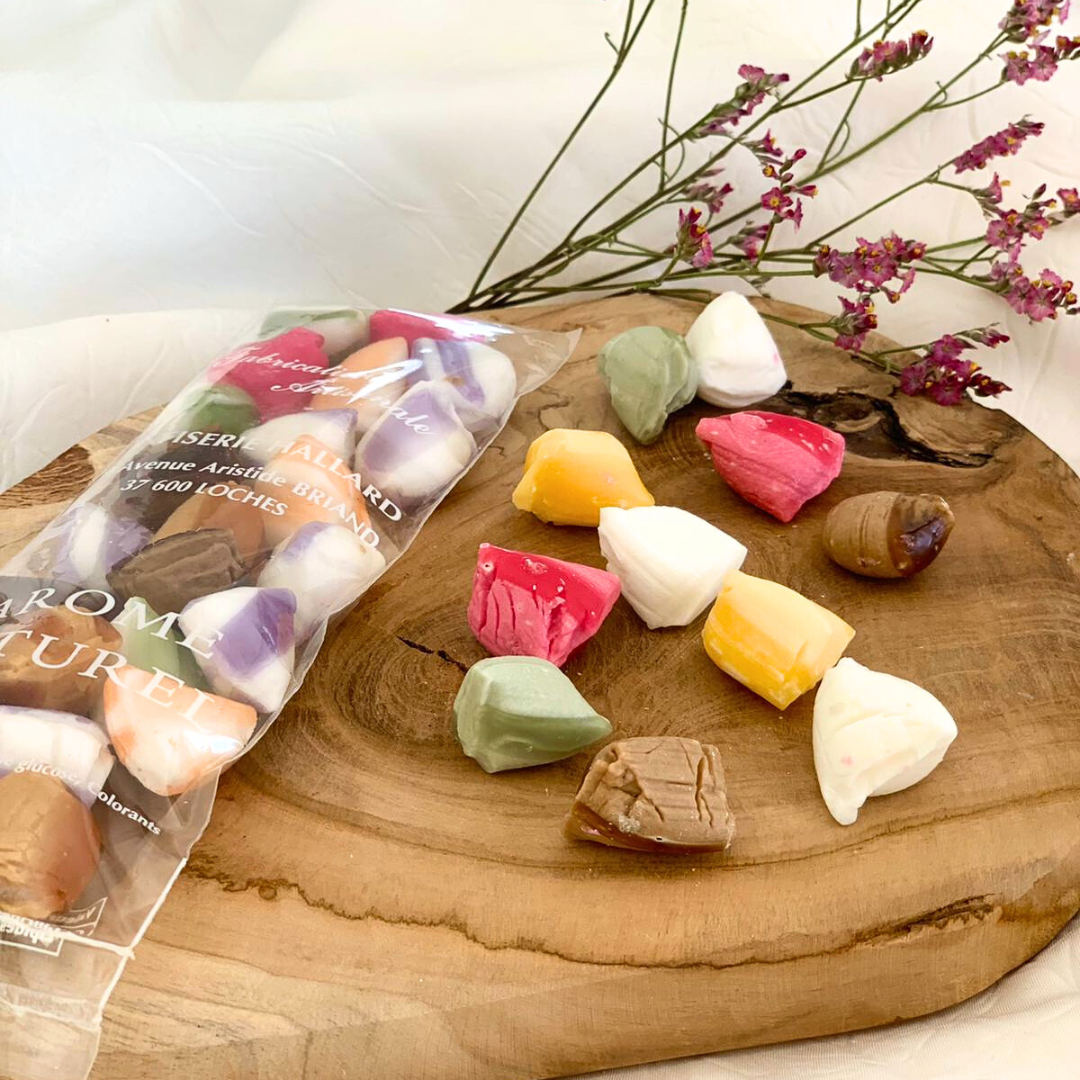 Berlingots personnalisés et régional Berlingots dans un sachet et éparpillés sur le côté, posés sur une planche en bois et fleurs en arrière-plan.