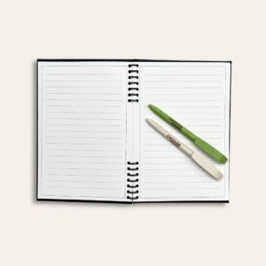 Un carnet avec deux stylos, un vert et un beige posés dessus.