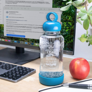 Gourde en verre incassable bleue, avec ordinateur crayon et pomme en arrière plan.