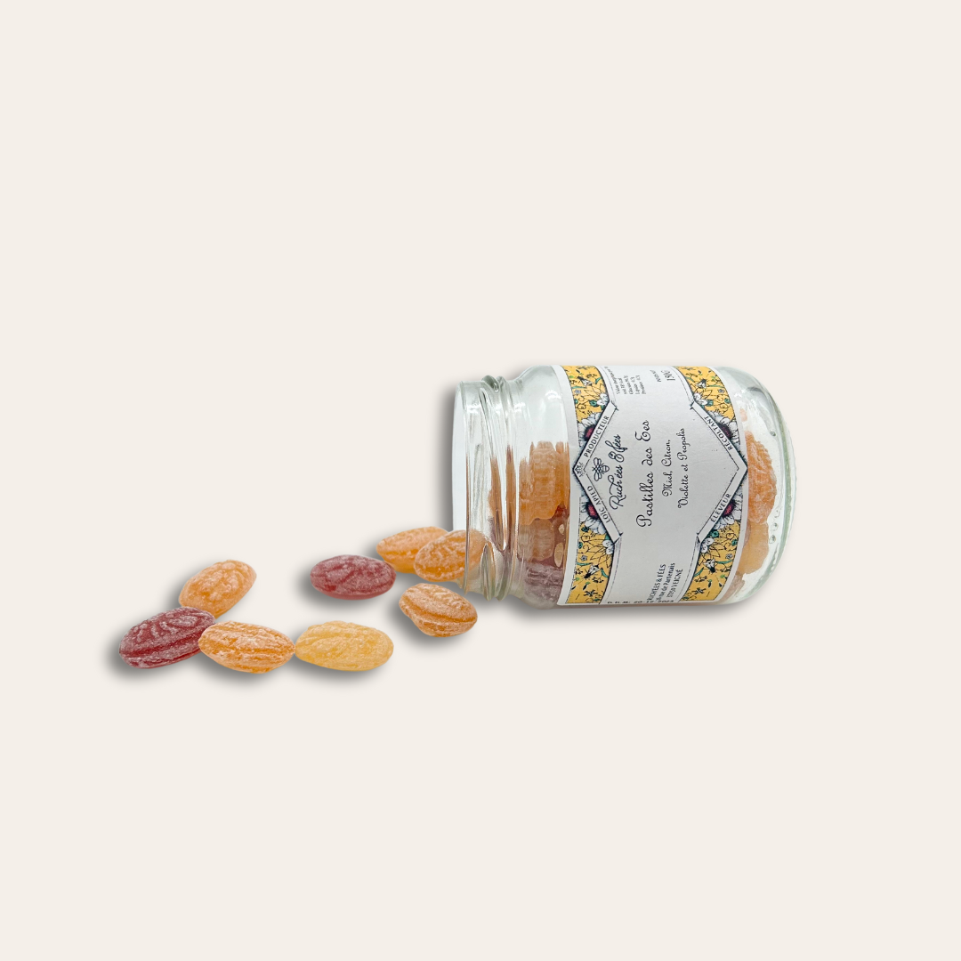 Pastilles miel régional Pot en verre avec une étiquette collée et rempli de pastilles miel citron puis des pastilles éparpillés.
