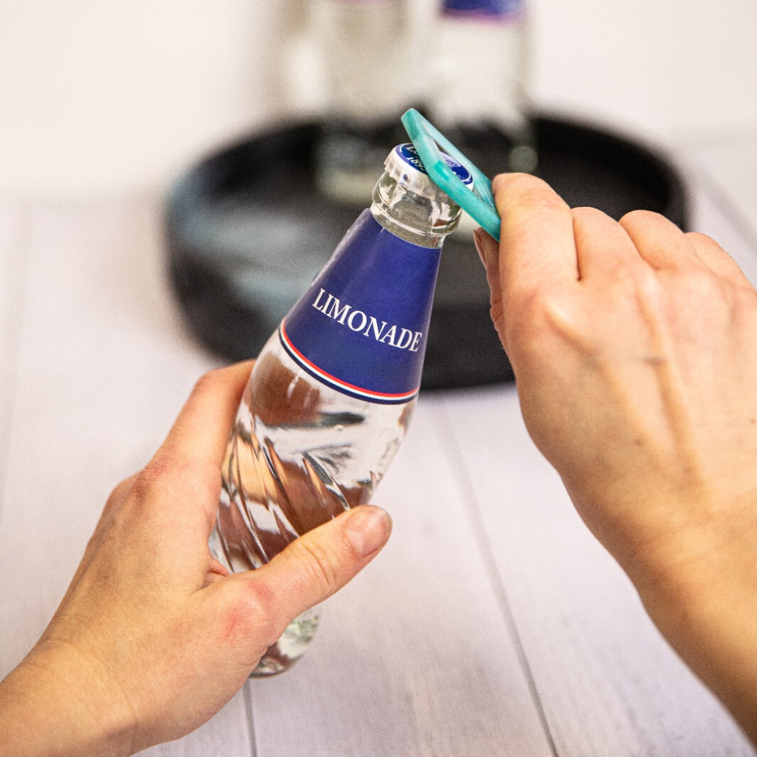 Porte-clé décapsuleur en plastique recyclé ouvrant une bouteille en verre.