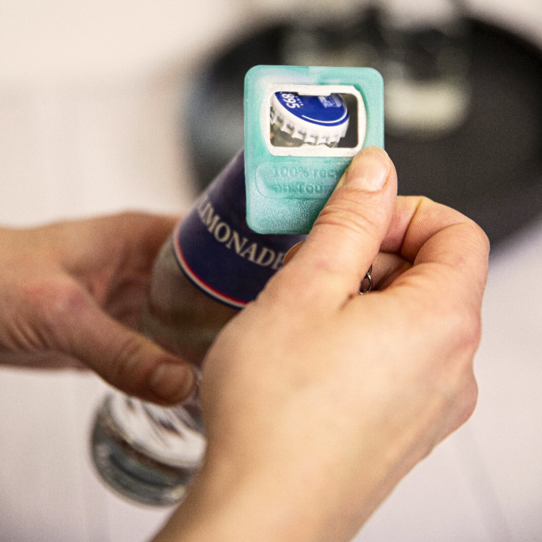 Zoom sur le porte-clé décapsuleur en plastique recyclé ouvrant une bouteille en verre.