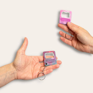 Deux mains tenant chacun un porte-clé décapsuleur en plastique recyclé rose et coloré.