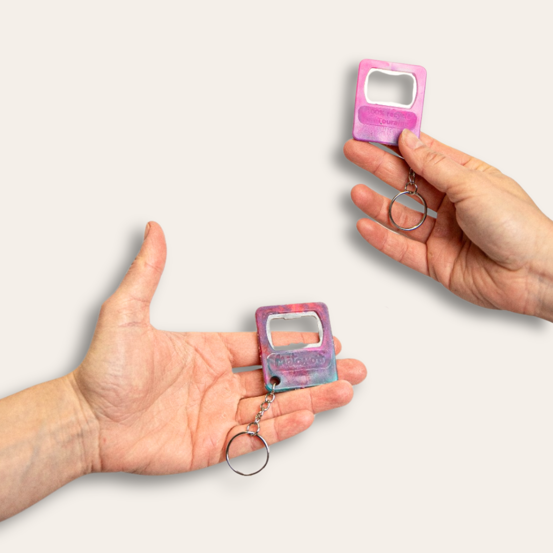 Deux mains tenant chacun un porte-clé décapsuleur en plastique recyclé rose et coloré.