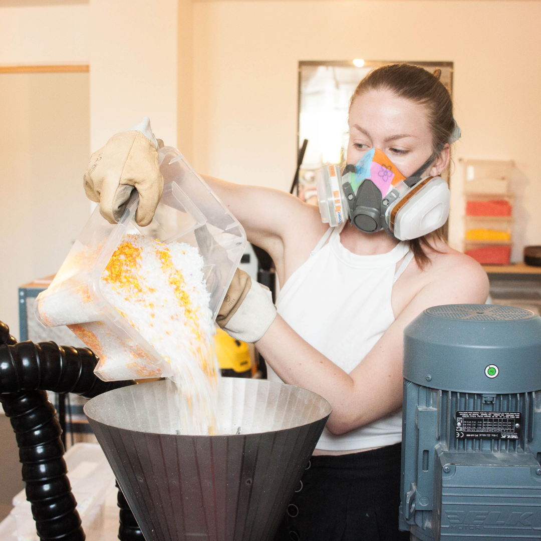 Femme remplissant des bouts de plastique dans une machine.
