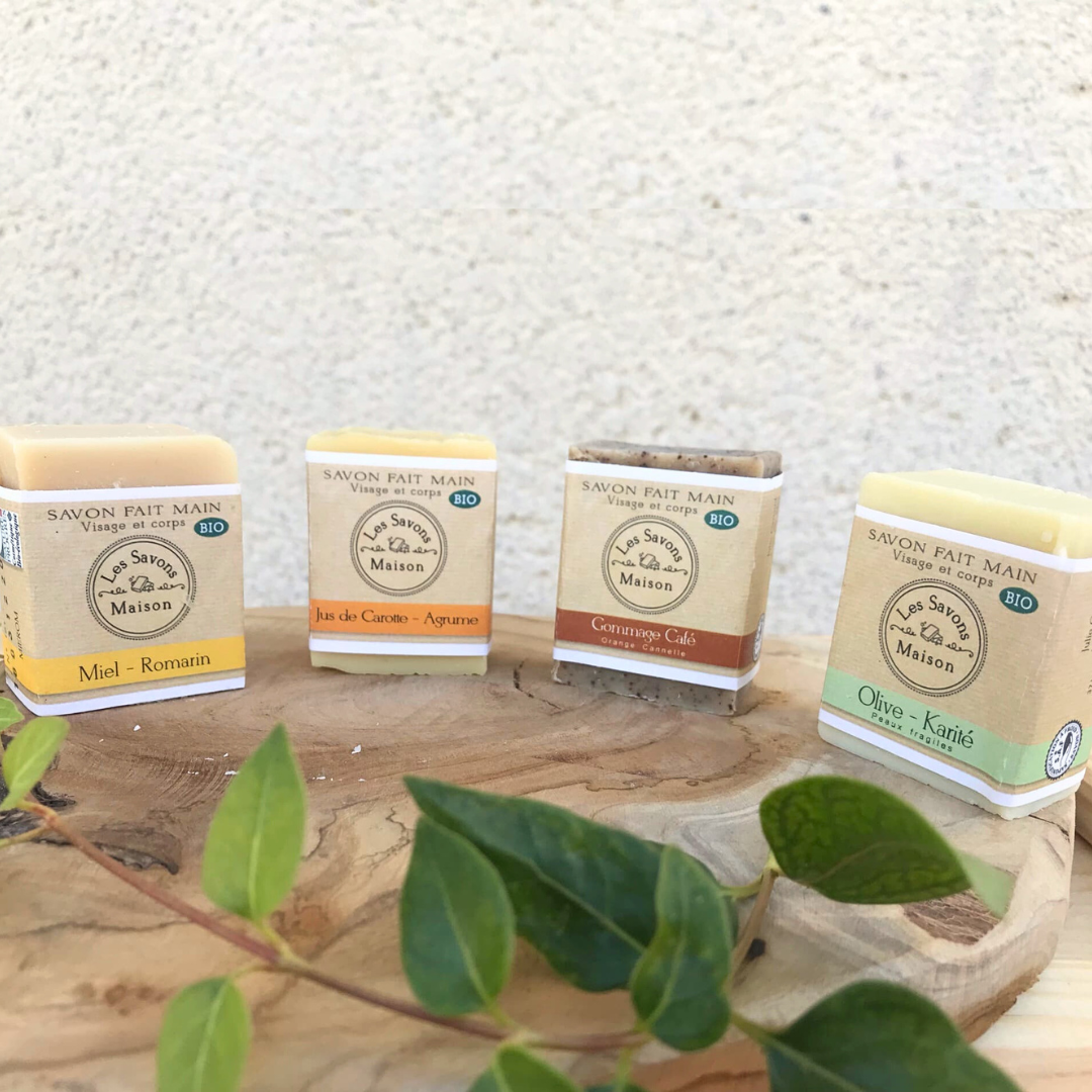 Savons Bio fait main à personnaliser 50g Quatre savons fait main et bio, posés sur une planche en bois avec feuilles.