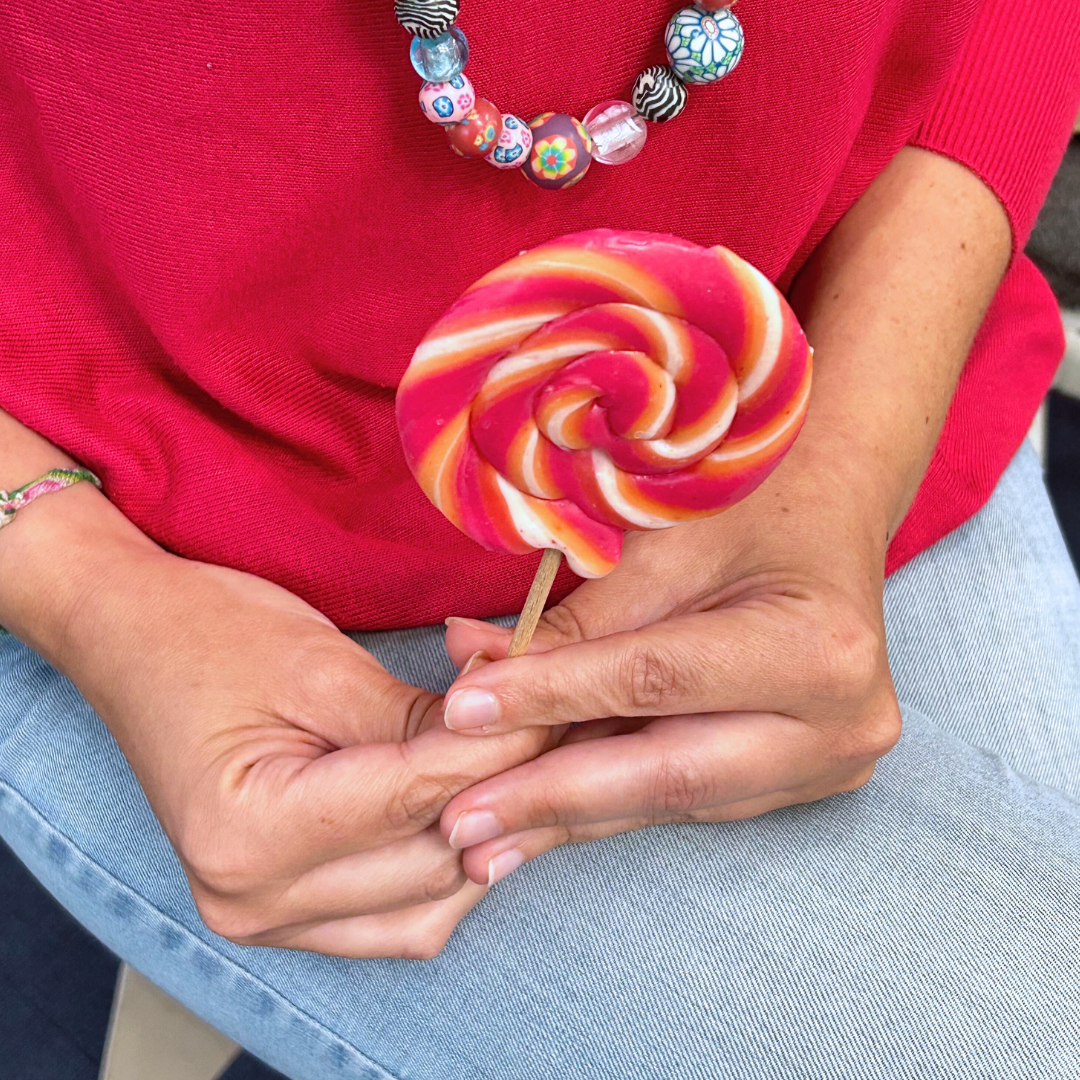 Mains tenant une sucette de couleur rose, orange et blanc.