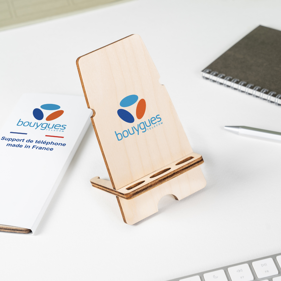 Support téléphone solidaire Bouygues Support de téléphone avec écrit Bouygues dessus, en arrière-plan un carnet, crayon et cartonnette.