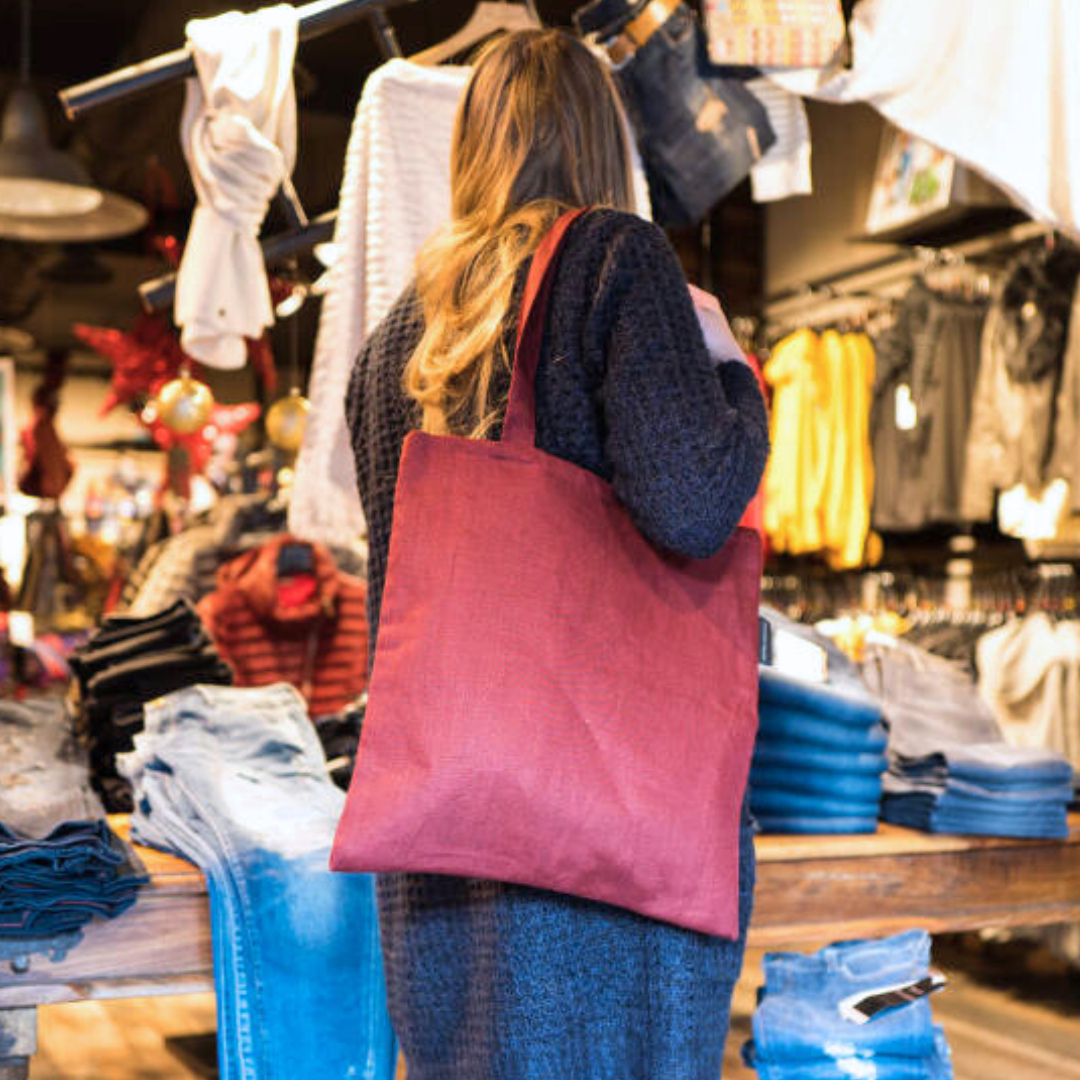 Tote bag plusieurs coloris Femme portant un tote bag rouge dans un magasin de textiles.