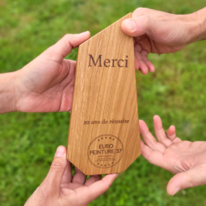 Trophée en bois tenu par des mains.